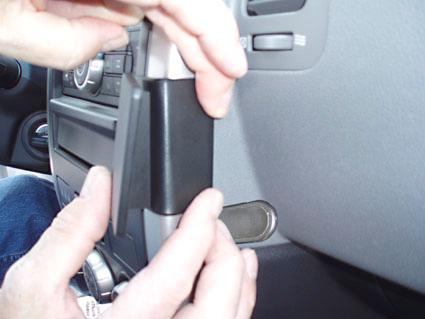 En person fäster en svart del på instrumentbrädan i en bil.