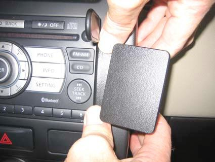 En hand håller en svart enhet vid bilens navigationssystem.