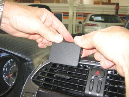 Två händer placerar en svart enhet på en bils instrumentbräda.