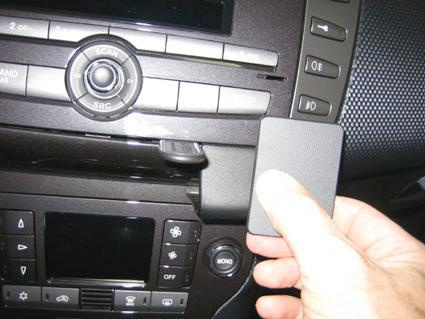 En hand håller en svart enhet som kopplas till bilens instrumentpanel.