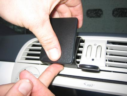 En hand fäster en svart komponent på en bils luftutlopp.