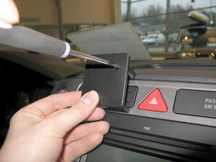 En hand håller en skruvmejsel mot en bilpanel med en svart fäste.