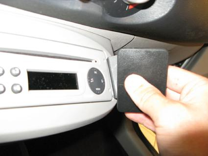 En hand som håller en svart plastbit vid bilens instrumentpanel.