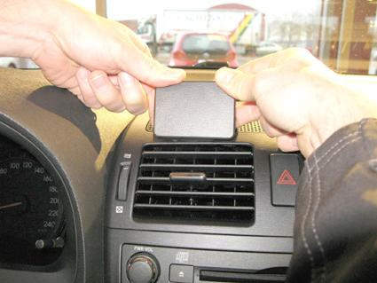 Två händer håller en svart platta över en luftventil i en bil.