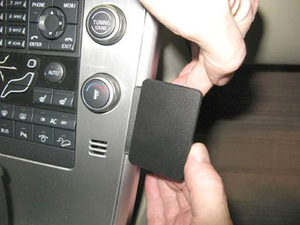 En hand tar bort en svart plastpanel från en bilinteriör.