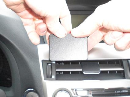 Två händer håller en svart, rektangulär del nära bilens luftventil.