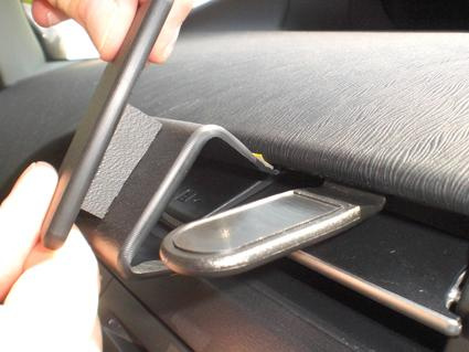 En hand som håller en telefon över en hållare i en bil.