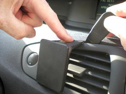 En hand fäster en del på en ventilationsgaller i bilen.