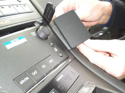 En hand håller en vinklad monteringsbygel på en bils instrumentpanel.