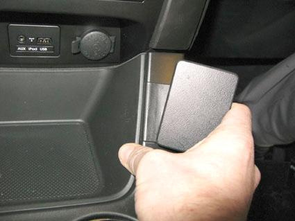 En hand håller i en svart plastdetalj inuti en bil.