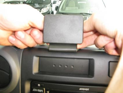 Händer installerar en svart enhet på instrumentbrädan i en bil.