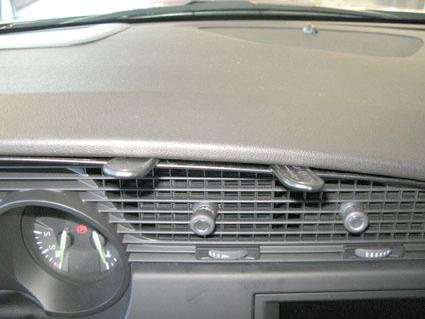 En bilinteriör med luftar, instrumentpanel och kontroller.