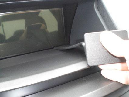 En hand håller i en liten svart del vid frontpanelen av en bil.