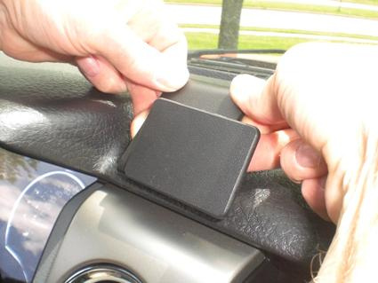 En person fäster en svart komponent på instrumentbrädan i en bil.