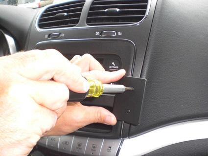 En hand håller en skruvmejsel mot ett bilinteriörsdel.