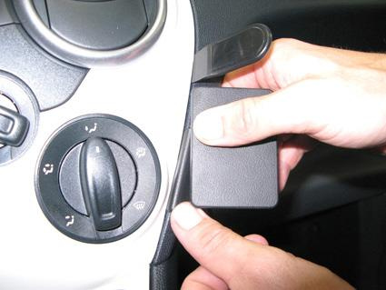 En hand som håller en svart kuvertformad del nära en ratt- eller kontrollpanel.