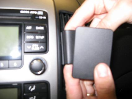 En person håller en svart del som verkar passa in i bilens instrumentpanel.