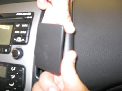 En hand som håller i en svart komponent nära instrumentpanelen i en bil.