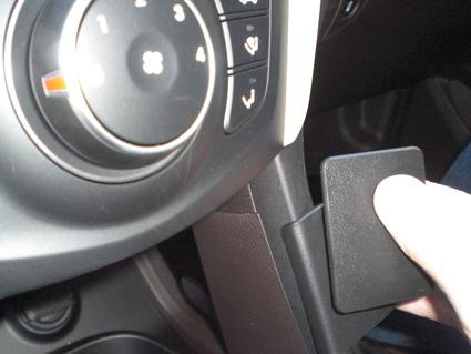 En hand som trycker på en svart knapp i en bilinteriör.