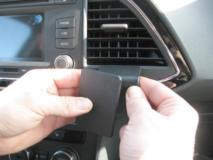 En hand håller en svart del som ska fästa vid luftutloppet i en bil.