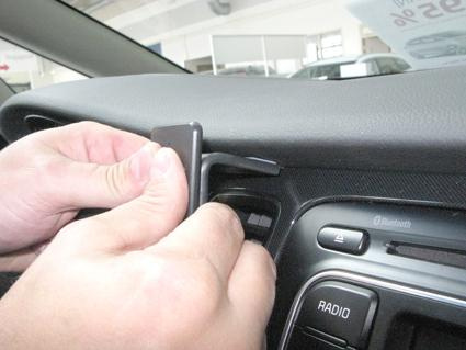 En person använder ett verktyg för att justera något på Kia Carens 14-15.