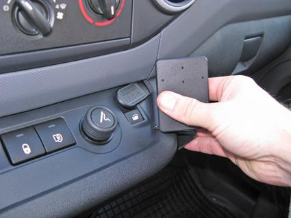 Hand som håller en svart enhet, placerad vid bilens kontrollpanel.