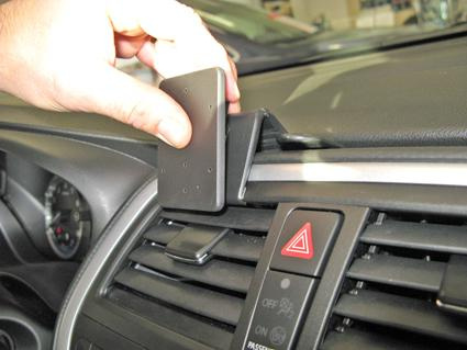 En hand håller i en svart enhet som fästs på bilens ventilationsgaller.