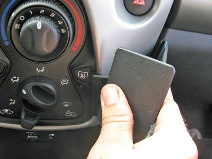 En hand håller i en svart enhet vid bilens luftkonditionering och kontroller.