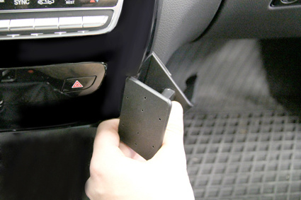 En hand som installerar ett vinklat svart tillbehör i bilen.