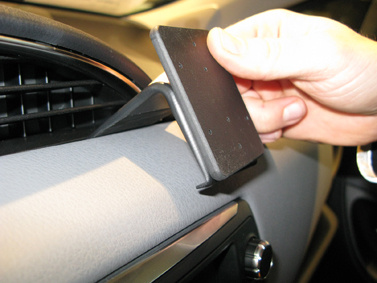En hand håller i en fäste för att montera något i en bilinteriör.