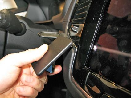 En hand håller en svart enhet i en bils inredning nära en skärm.