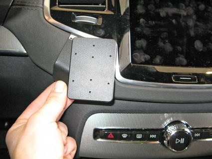 En svart plastdel som hålls i handen, kopplad till en bilinteriör.