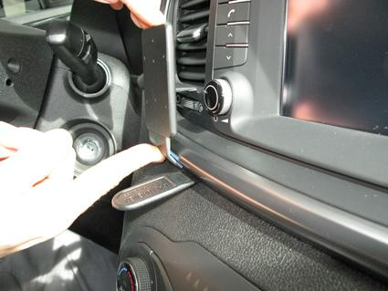 En hand pekar på en del av bilens interiör med kontroller och skärm.