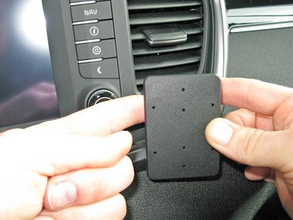 En hand håller en monteringsbygel vid en bils instrumentpanel.