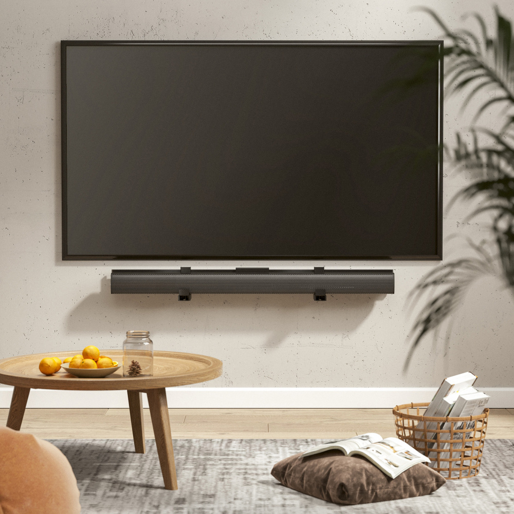 En TV är monterad på väggen ovanför en soundbar och en rund träbord.