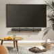 LogiLink Universalfäste för soundbar, 86-155 mm djup En TV är monterad på väggen ovanför en soundbar och en rund träbord.