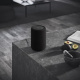 Audio Pro A10 MKII aktiv Wifi-högtalare, svart styck Svart högtalare på en stenliknande yta med frukt och tidningar i bakgrunden.