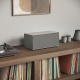 Audio Pro C20 högtalare med AirPlay 2, HDMI & mer, grå En grå högtalare på ett bord med vinylskivor, en skivspelare och några dekorativa föremål.