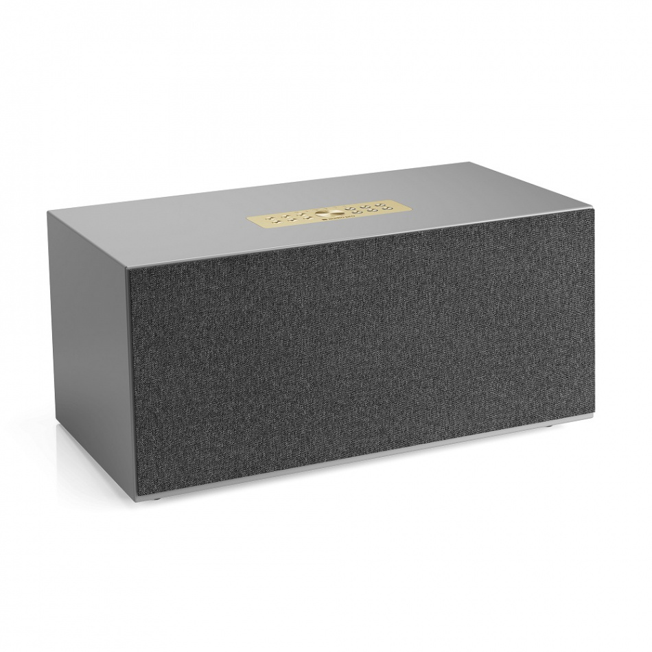 En grå högtalare med tygfront och guldfärgad logotyp.