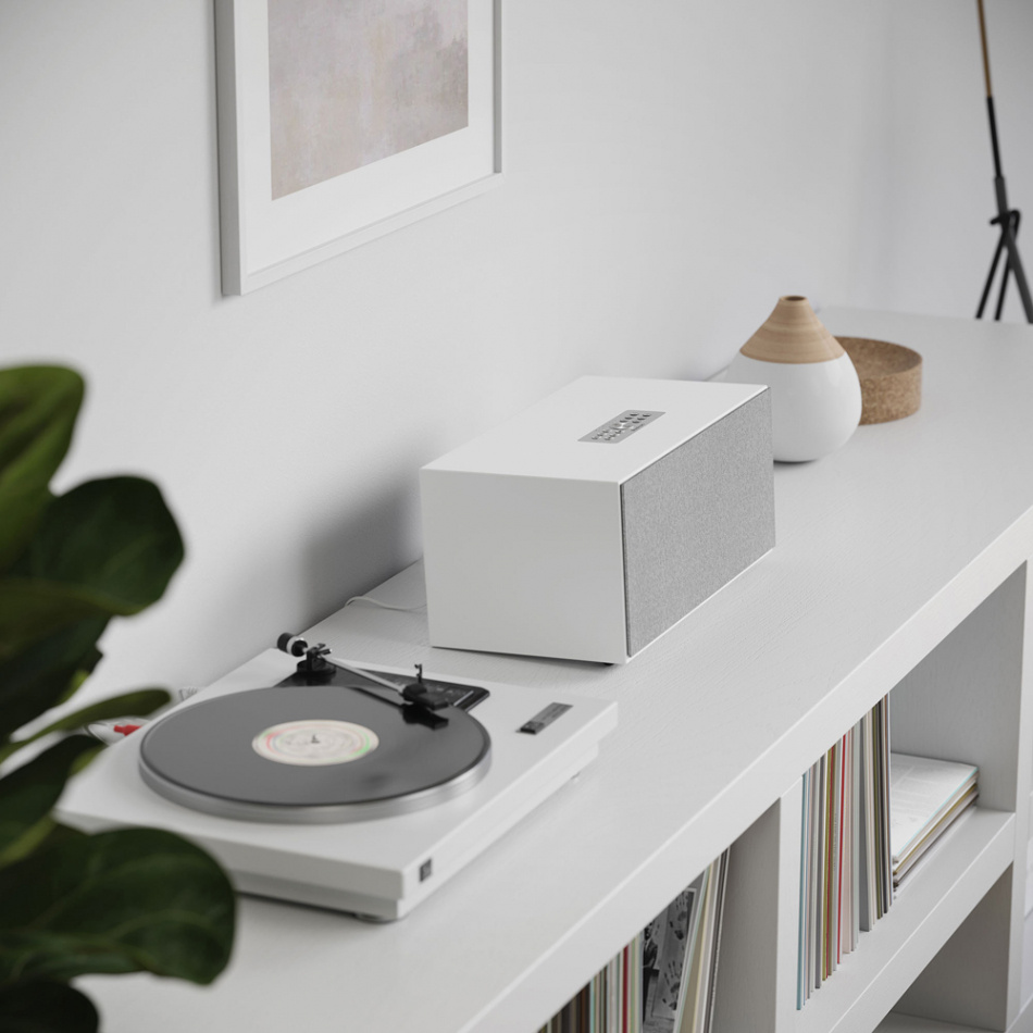 Vit högtalare bredvid en skivspelare på ett modernt sideboard.