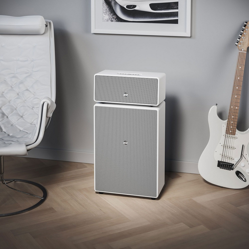 Vit högtalare med två sektioner, modern design, placerad i ett rum med gitarr.