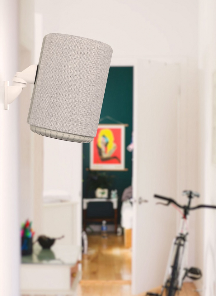 En ljusgrå smarthögtalare monterad på väggen i ett modernt rum.