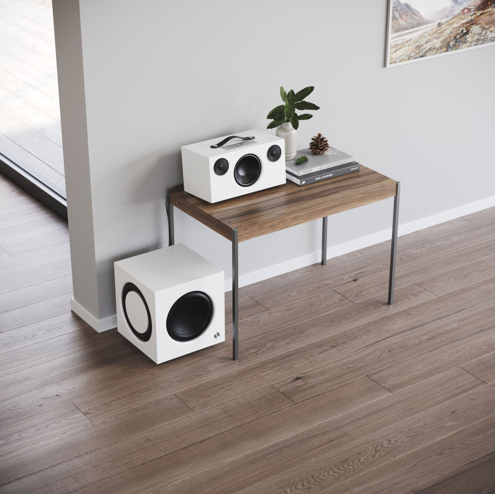 En vit aktiv subwoofer och högtalare på ett bord i elegant inredning.