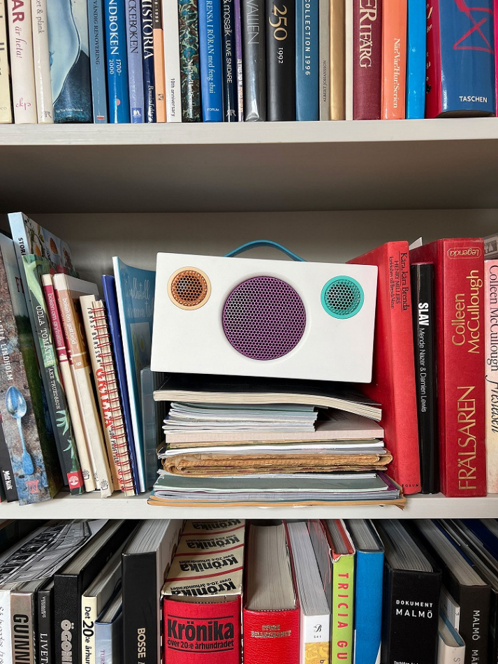 En Bluetooth-högtalare ovanpå böcker i en bokhylla.