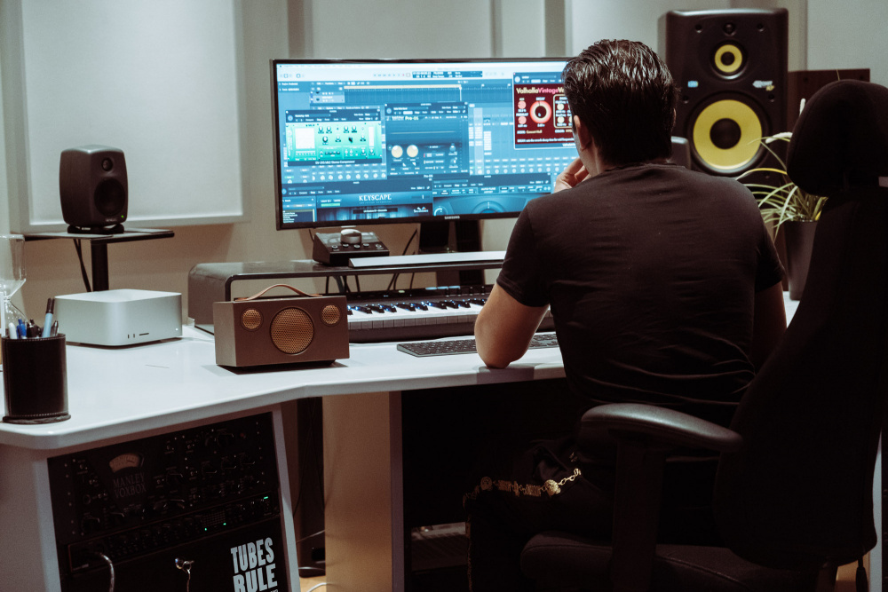 En person arbetar i ett musikstudio med en dator och Audio Pro Addon T3+ högtalare.