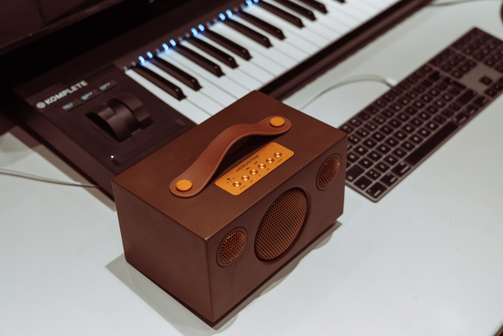 En brun Bluetooth-högtalare med handtag och kontroller, placerad på ett skrivbord.