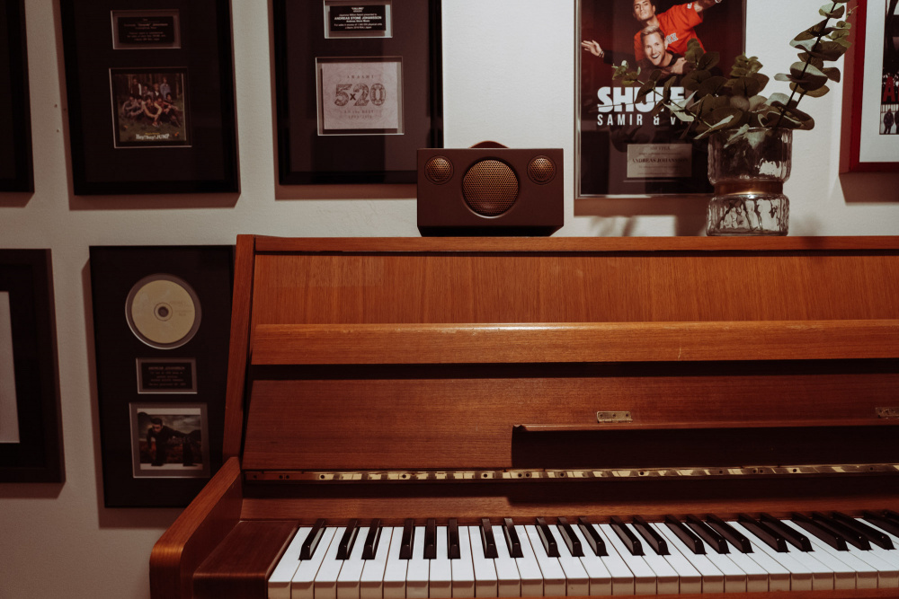 En Bluetooth-högtalare ovanpå ett piano med tavlor på väggen.