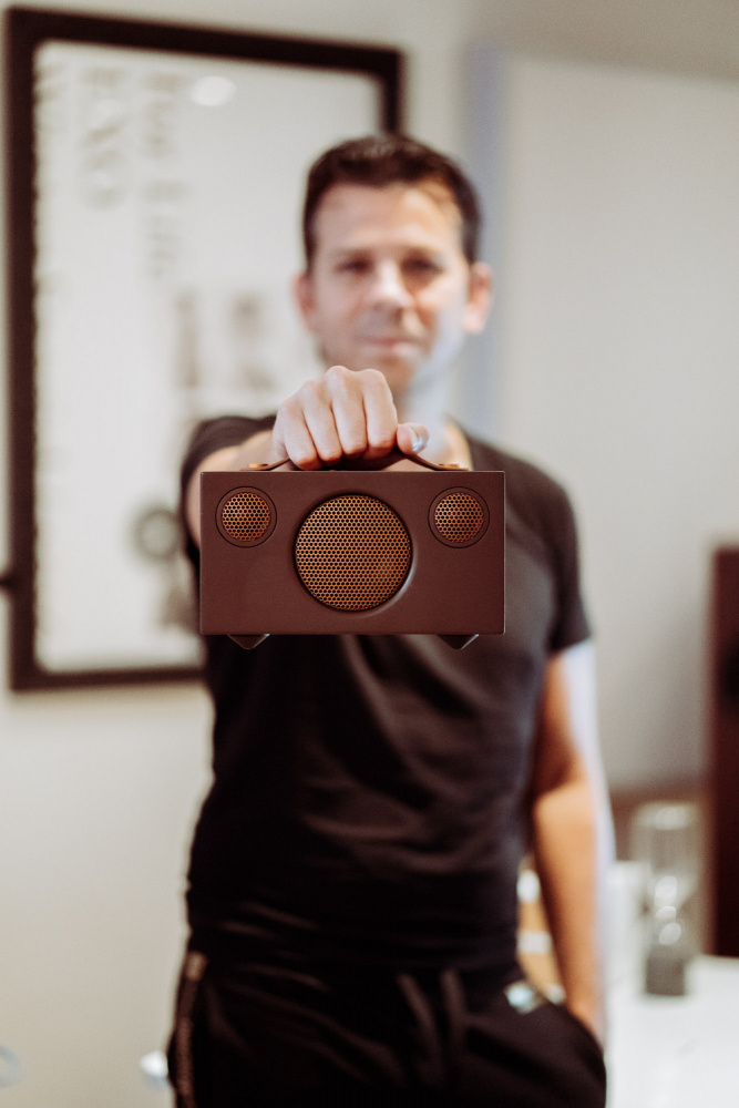 En man håller upp en kompakt Bluetooth-högtalare i brun färg.