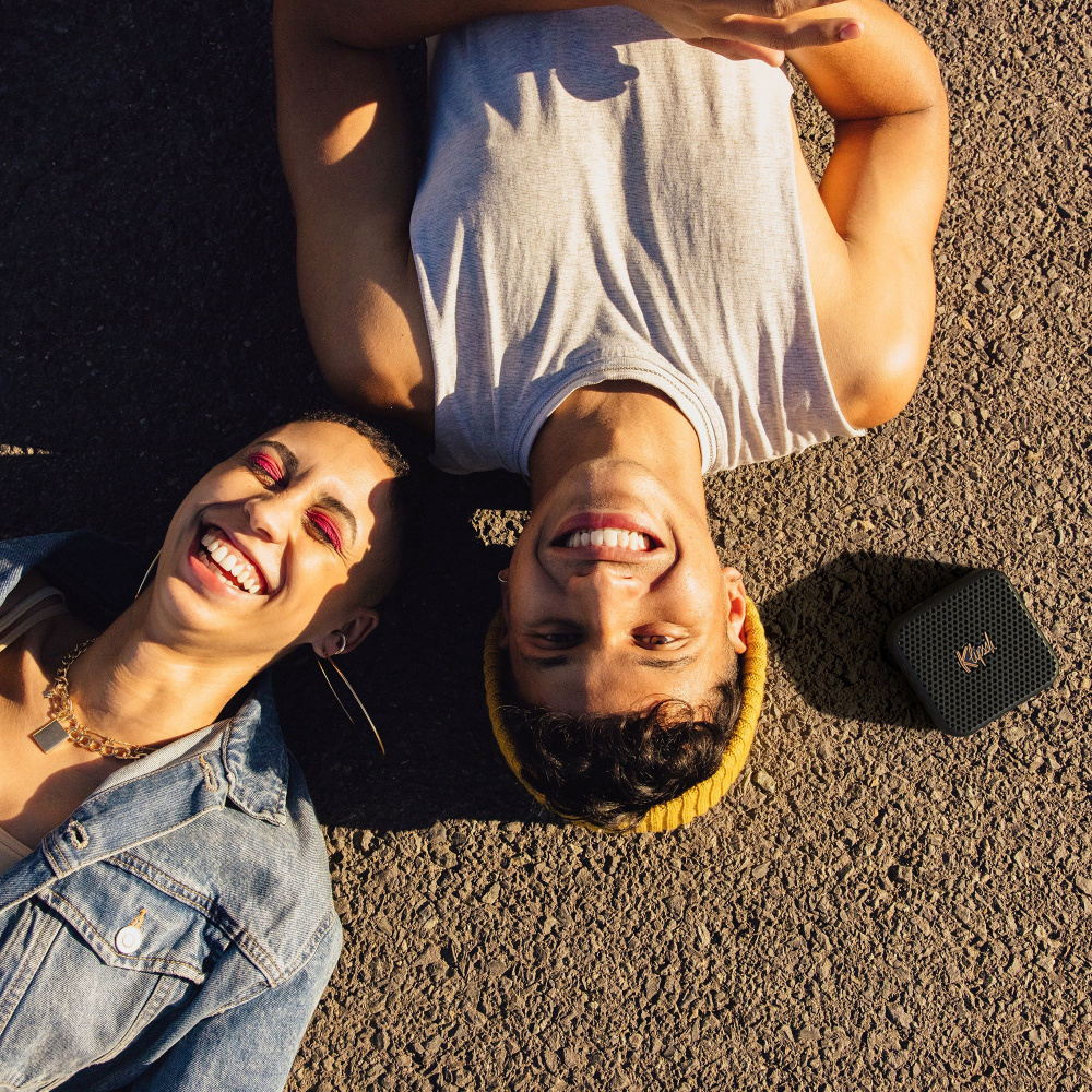 Två leende personer ligger på marken med en högtalare bredvid sig.