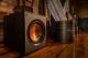 Klipsch R-120SW aktiv subwoofer, svart En svart subwoofer med en kopparfärgad högtalare, placerad i en inomhusmiljö.